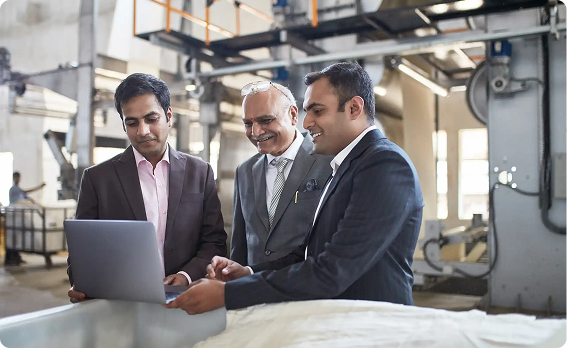 Three colleagues reviewing compliance data on a laptop in a factory