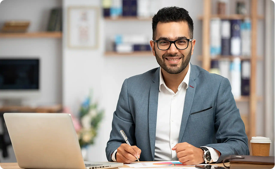 Professional working on a laptop with reports at his desk